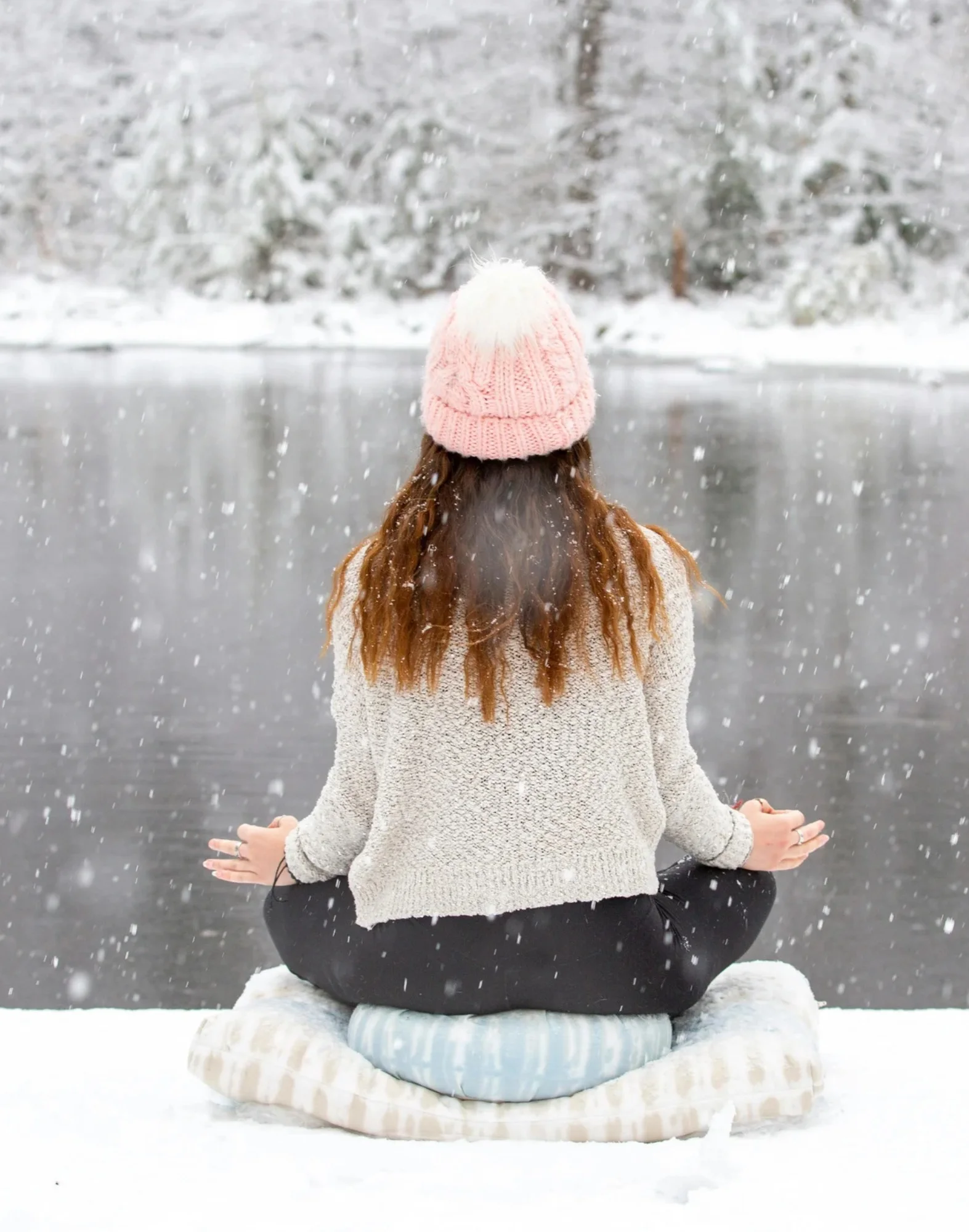 Frau meditiert im Schnee an einem See in winterlicher Landschaft